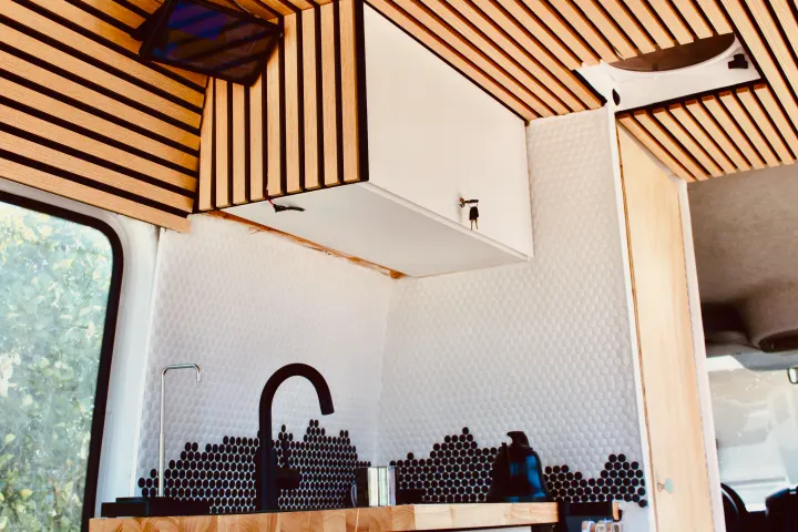 Stylish RV rental kitchen with slatted wood ceiling, unique white and black honeycomb tile backsplash, and a modern black faucet.. Mercedes-Benz Sprinter 2008