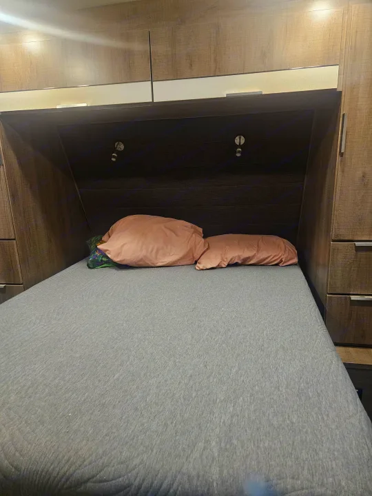Comfortable RV rental bedroom features a grey bed, pink pillows, and warm-toned built-in cabinetry with reading lights.. Imagine Imagine design 2020