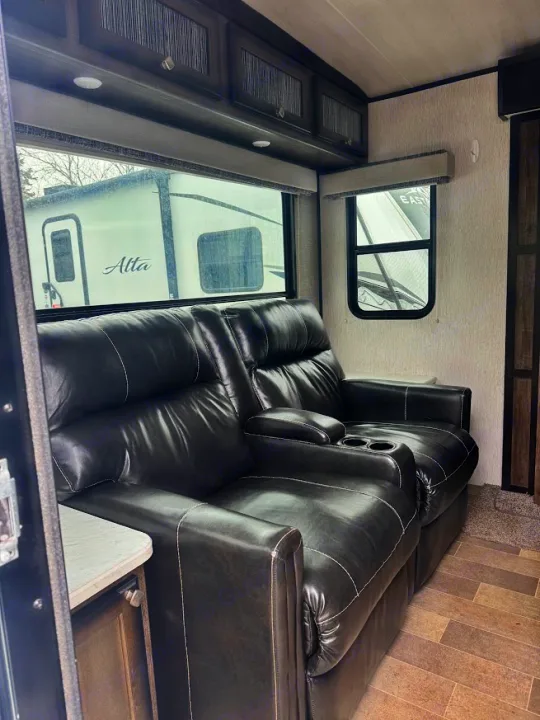 Comfortable RV rental living area with a dark leather recliner sofa, overhead cabinets, and large windows.. Heartland RVs Mallard 2019