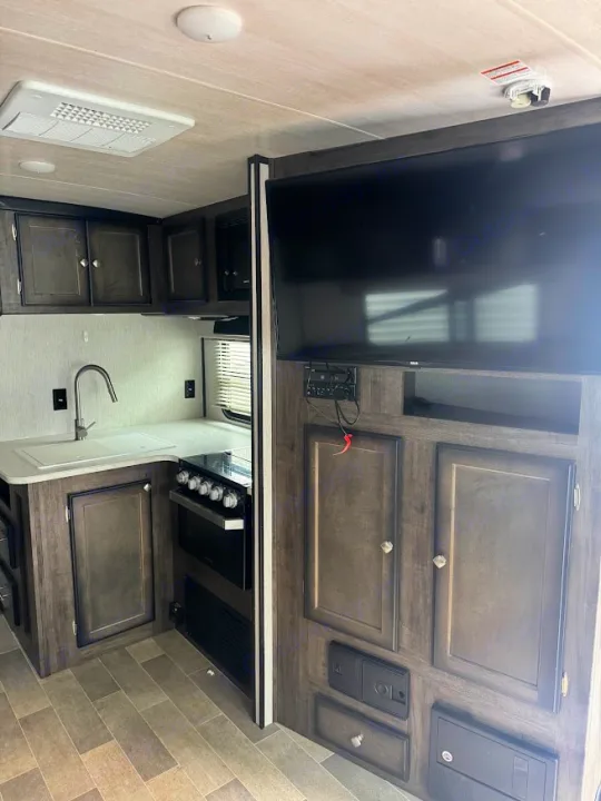Spacious RV rental interior featuring a modern kitchenette with sink, stove, microwave, and an entertainment center with a large TV.. Heartland RVs Mallard 2019