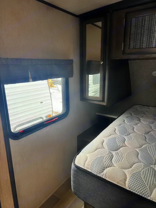An RV rental bedroom with a comfortable mattress, window with blinds, and a mirrored cabinet, showing an emergency exit.. Heartland RVs Mallard 2019