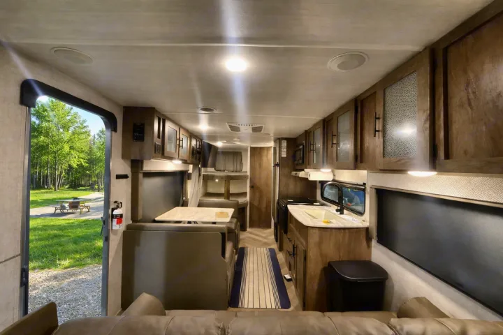 Bright RV rental interior showing kitchen, dinette, bunk beds, and a beautiful outdoor campsite view through the open door.. Forest River Salem Cruise Lite 2020