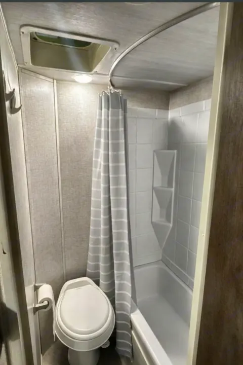 Inside an RV rental bathroom featuring a white toilet, compact shower/tub with a striped curtain, and ceiling vent.. Forest River Salem Cruise Lite 2020