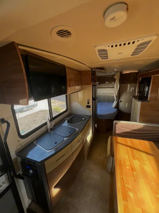 RV rental interior: View of the kitchen, dining booth with wooden table, a rear bed, and mounted TV.. Winnebago View 2016