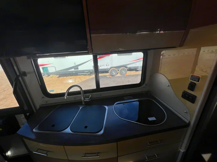 RV rental kitchen: sleek counter with covered double sink, glass stovetop, and window view. Compact camper interior.. Winnebago View 2016
