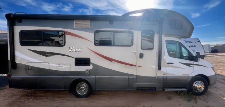 Side view of a cream and gray Winnebago View Class C motorhome for rv rental, parked outdoors on a sunny day.. Winnebago View 2016