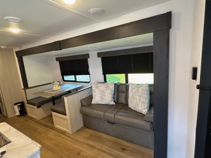 Spacious RV rental living area with light wood dinette, grey sofa, and dark window blinds, offering a comfortable space.. Forest River Palomino Puma Camping Edition 2025