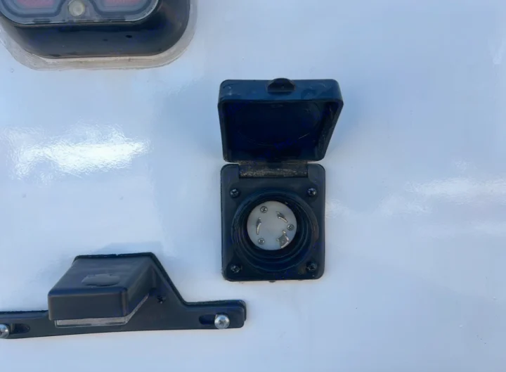 RV rental's shore power electrical inlet is open on a white exterior, revealing the pins for power connection.. Coachmen Freelander 2021