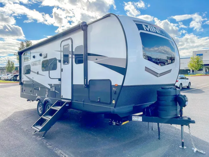 This white and gray Minilite travel trailer, ideal for an RV rental, is parked with its steps down, ready for adventure.. Forest River Rockwood Mini Lite 2024
