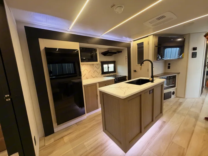 Sleek RV rental kitchen featuring a central island, black appliances, light flooring, and bright ceiling & under-island lighting.. Forest River Salem Hemisphere 2026