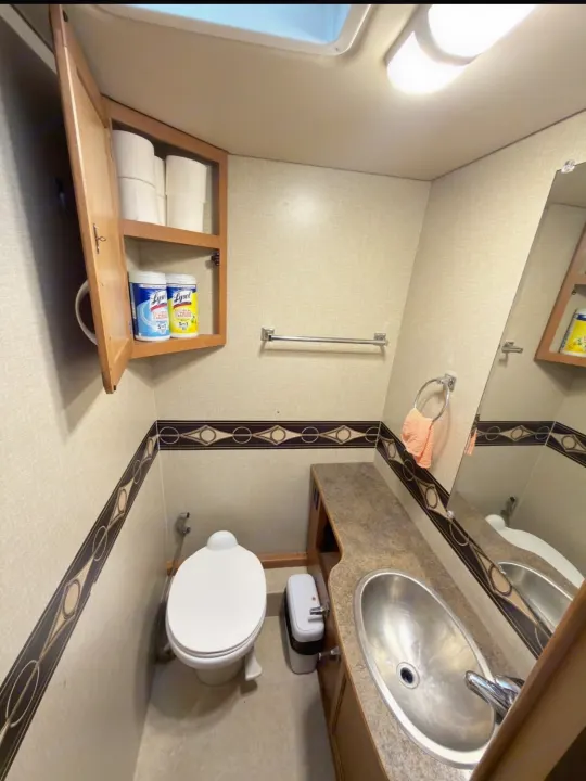 Clean and functional RV rental bathroom featuring toilet, sink, mirror, cabinet with supplies, and small trash bin.. Winnebago Minnie Winnie 2015