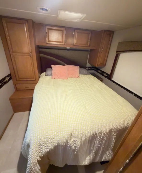 Cozy RV rental bedroom with a queen bed, ample storage cabinets, and a large window, ready for your next adventure.. Winnebago Minnie Winnie 2015