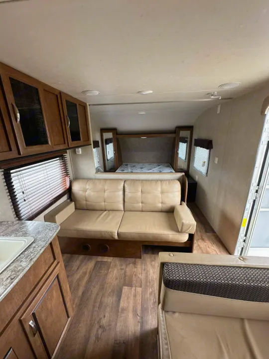 This RV rental interior offers a comfortable tan sofa, a bed, kitchen counter, overhead cabinets, and wood flooring.. Forest River Salem Cruise Lite 2016