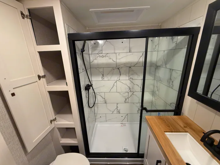 Compact RV rental bathroom featuring a modern tiled shower, wooden vanity, black fixtures, and built-in storage.. Jayco Eagle 2025