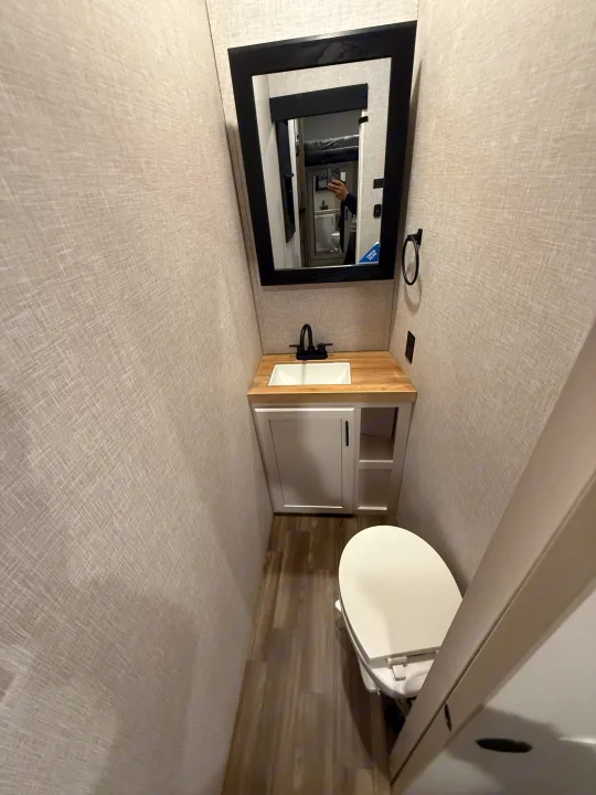 This narrow RV rental bathroom features a sink, mirror, and toilet, with light textured walls and wood-look flooring.. Jayco Eagle 2025
