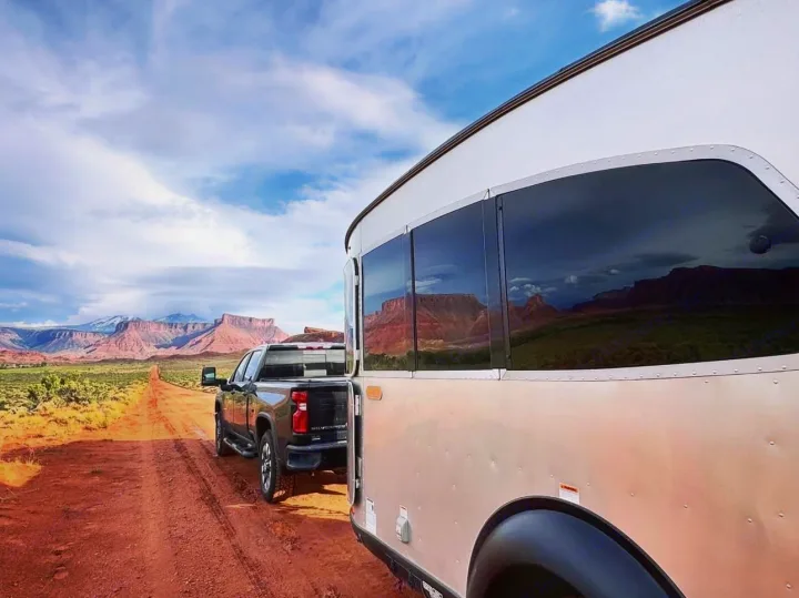 Scenic RV rental journey: Truck towing a travel trailer on a dirt road through a desert landscape with red mountains.. Toyota Tundra TRD Off Road 2026