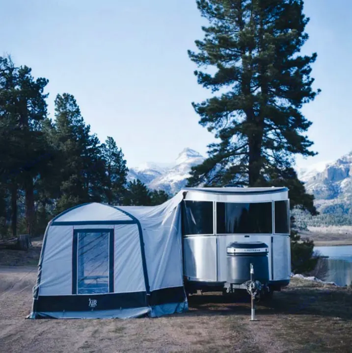 Enjoy a scenic Airstream RV rental with an attached tent, parked by a lake amidst pine trees and snowy mountains.. Toyota Tundra TRD Off Road 2026