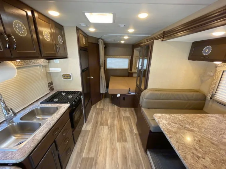 RV rental interior: modern kitchen with dual sinks & stove, cozy dinette, and sleeping area. Wood-look floors, bright lighting.. Thor Freedom Elite 2018