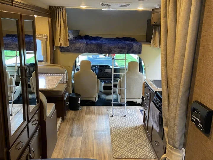 Spacious rv rental interior showing an overhead bunk bed, front cab, dinette, and compact kitchen area.. Thor Freedom Elite 2018