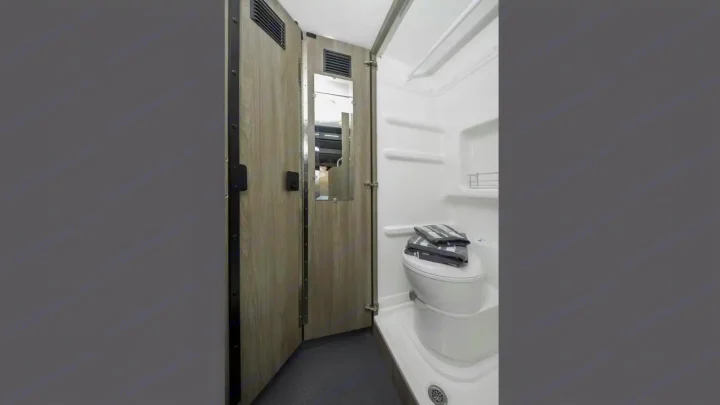 This RV rental wet bath features a toilet, shower, and mirror on the door, offering essential amenities in a compact space.. Winnebago Solis 2024