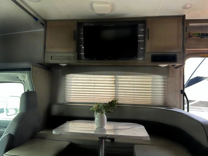 RV rental interior featuring a cozy dinette with U-shaped seating and a TV entertainment center above the window.. Coachmen Freelander 2021