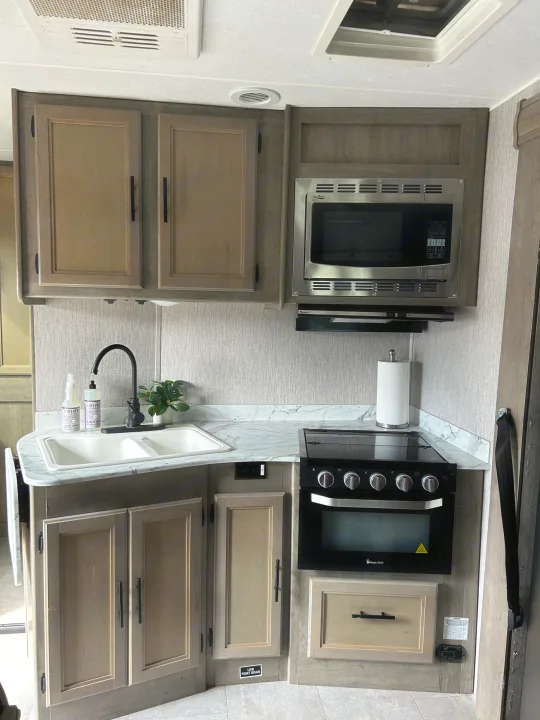 This RV rental boasts a functional kitchen with a double sink, black faucet, microwave, stove, and light wood cabinetry.. Coachmen Freelander 2021