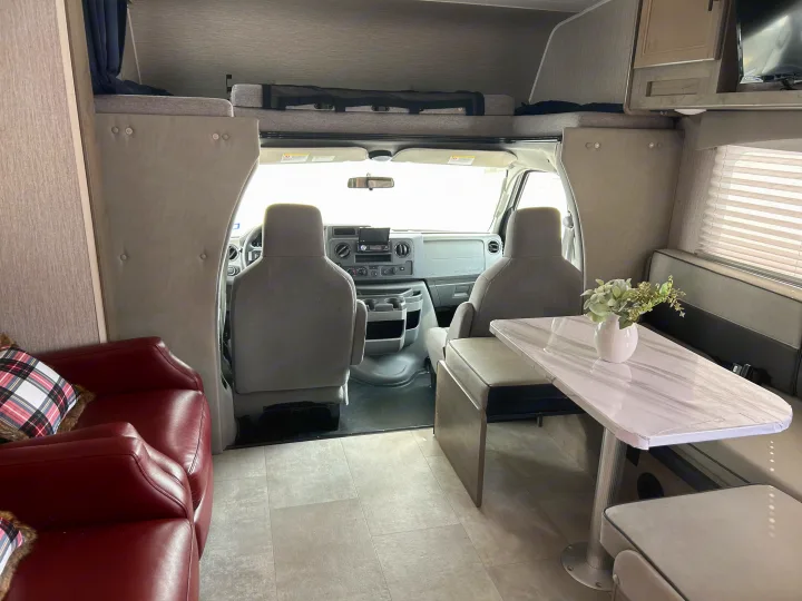 Spacious rv rental interior featuring a cozy dining area, driver's cockpit, and overhead bunk for comfortable travel.. Coachmen Freelander 2021