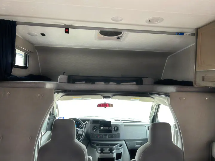 Inside an rv rental, featuring the front driver's area and a comfortable overhead bunk with a safety net.. Coachmen Freelander 2021