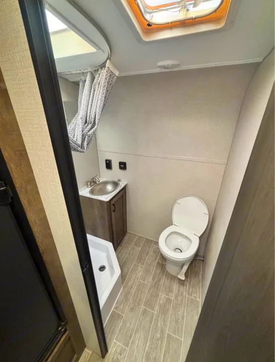 This rv rental bathroom features a compact shower, toilet, and sink. Note the ceiling skylight for natural light.. Sonic Lite 2021