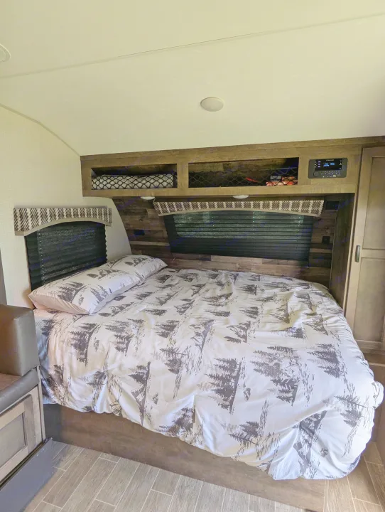 RV rental bedroom features a cozy bed with nature-themed bedding, overhead storage, and an entertainment system.. Sonic Lite 2021