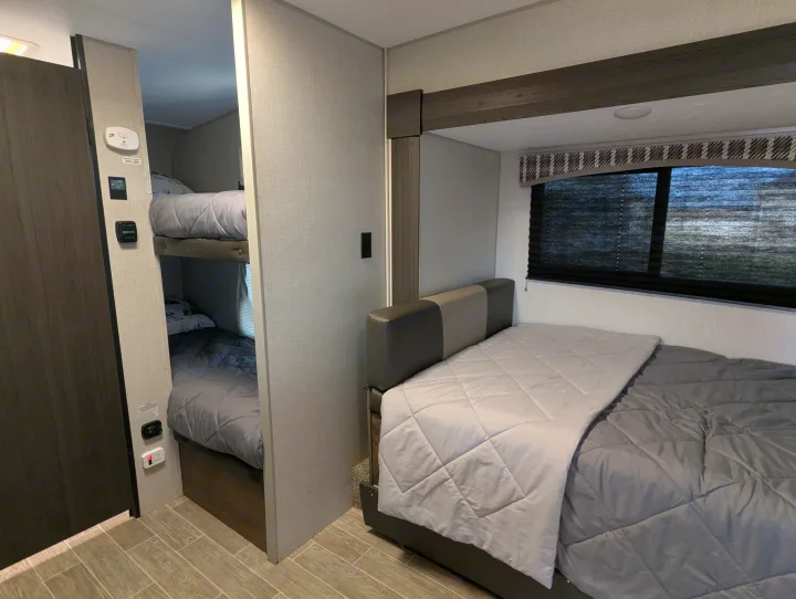 Comfortable RV rental interior featuring a cozy main bed, bunk beds, and essential controls for a pleasant stay.. Sonic Lite 2021