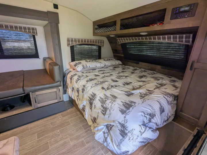 Cozy rv rental bedroom interior featuring a bed with nature-themed bedding, a compact dinette, and overhead storage.. Sonic Lite 2021