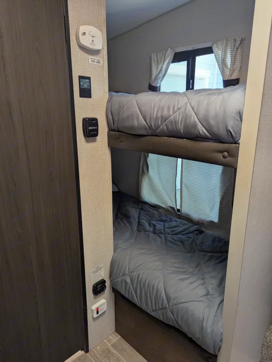 Cozy bunk beds in an RV rental, featuring windows, a 250 lbs capacity sign, thermostat, and smoke detector.. Sonic Lite 2021
