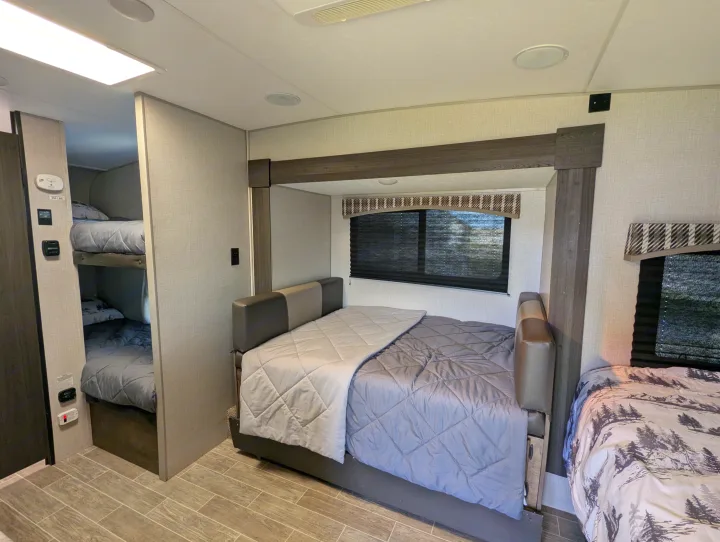 Rv rental interior: main bed with gray comforter, bunk beds, and a nature-themed bed, providing ample sleeping for guests.. Sonic Lite 2021