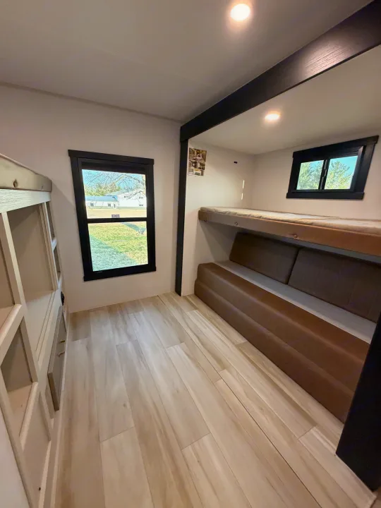 This RV rental bunk room features light wood-look floors, built-in bunk beds on each side, a brown sofa, and large windows.. Forest River Salem Hemisphere 2026