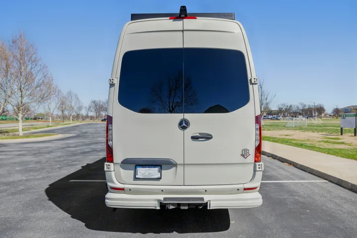 Rear view of a white Mercedes Sprinter van, a perfect RV rental, parked on asphalt with a field and trees in the background.. OGV Luxury Coach V-Cruise 2026
