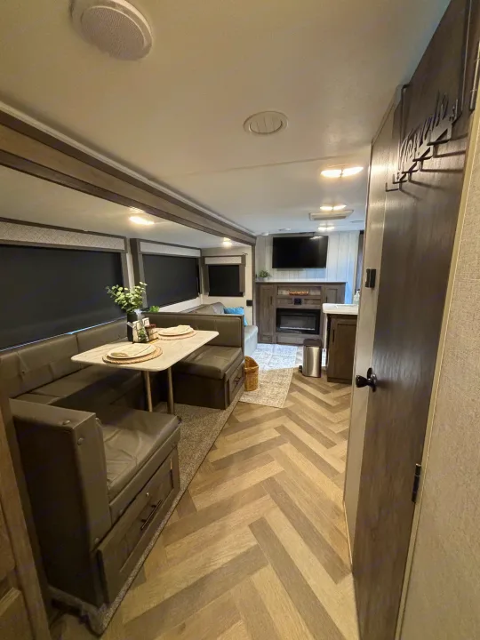 Modern RV rental interior with a cozy dinette, fireplace, TV, and stylish herringbone flooring, perfect for travel.. Forest River Wildwood 2020
