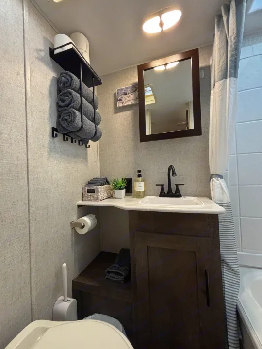 Clean and organized compact RV rental bathroom with vanity, sink, toilet, and towel storage solutions.. Forest River Wildwood 2020