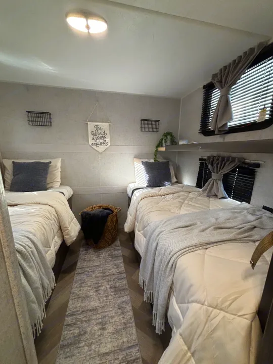 Cozy RV rental bedroom with two side-by-side beds, neutral decor, and travel-themed accents for a comfortable journey.. Forest River Wildwood 2020