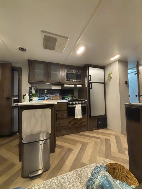 This RV rental features a modern, compact kitchen with a stove, microwave, fridge, and stylish herringbone floor.. Forest River Wildwood 2020