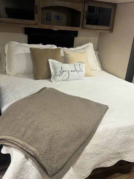 Cozy RV rental bedroom with white quilted bedding, neutral pillows, and a soft grey blanket. Overhead cabinets provide storage.. Sport Trek Touring Edition 2023