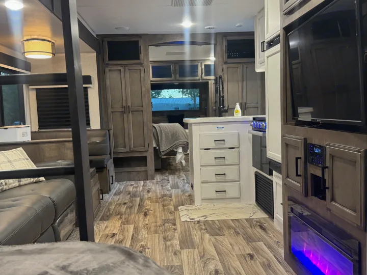 This modern RV rental interior showcases a kitchen island, entertainment unit with a fireplace, dinette, and wood-look floors.. Sport Trek Touring Edition 2023