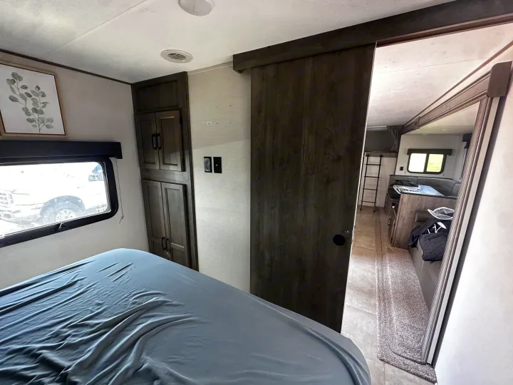 Cozy RV rental bedroom with bed, window, storage, and sliding door to living area with dinette and bunk ladder.. Coachmen Apex 2021