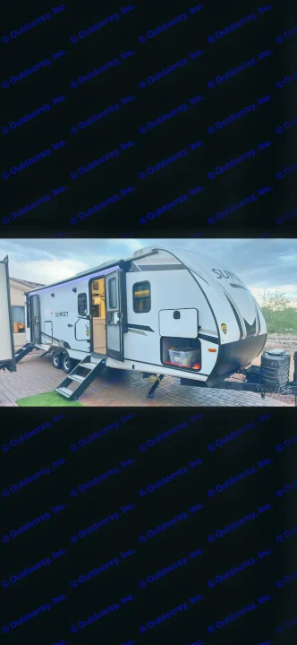 Experience comfort with this rv rental: a white travel trailer, open door showing a lit interior & blue-lit awning.. Keystone RV Sunset Trail 2024