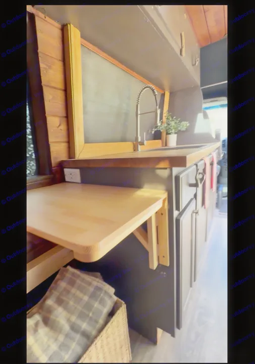 This RV rental interior shows a compact kitchen with a sink, wooden counter, and a fold-down table. A basket with a blanket sits below.. Mercedes Sprinter 2008