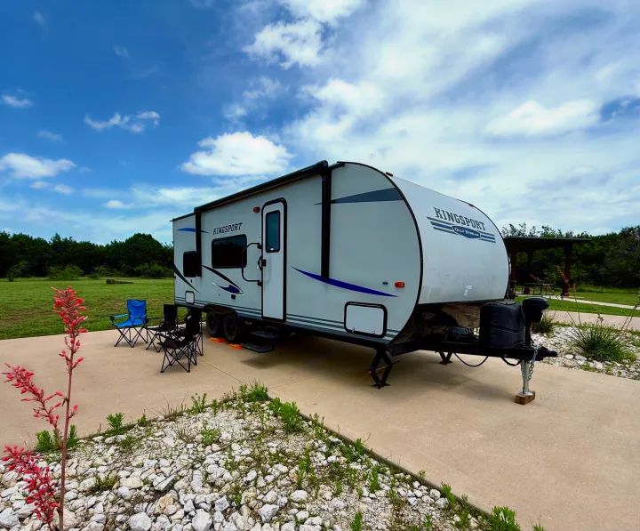 A Kingsport travel trailer RV rental is parked at a serene campsite with chairs, ready for a peaceful camping getaway.. Gulf Stream Kingsport 2021