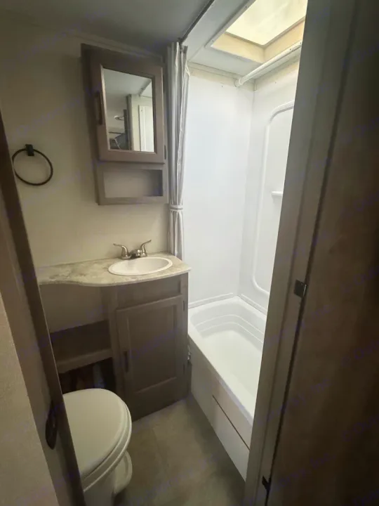 Clean RV rental bathroom with a toilet, sink vanity, mirrored cabinet, and a full tub/shower combo under a skylight.. Coachmen Apex 2021