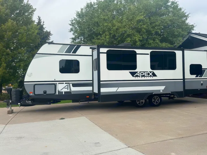 This modern white and grey Apex Ultralite travel trailer, with its side extended, is ready for your next rv rental adventure.. Coachmen Apex 2021