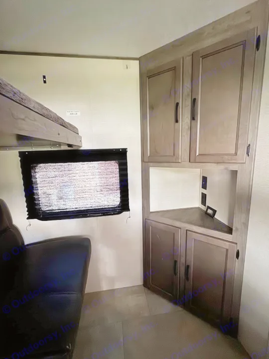 Cozy RV rental interior featuring a bunk bed, window with blind, and a functional corner cabinet unit with storage and outlets.. Coachmen Apex 2021