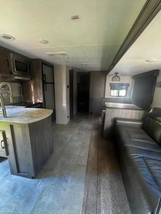 Modern RV rental interior with a gray kitchen island, dinette, and sofa. Features mixed flooring for a comfortable stay.. Coachmen Apex 2021